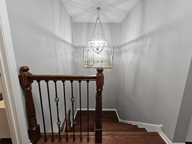 staircase with wood finished floors, an inviting chandelier, and baseboards