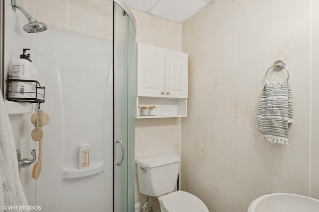 bathroom featuring tile walls, toilet, a shower stall, and a paneled ceiling