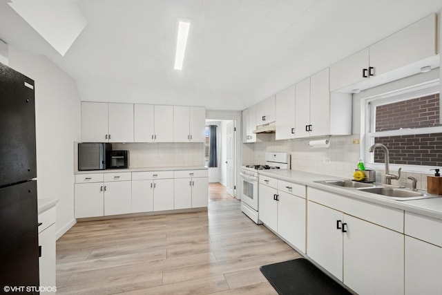 kitchen featuring white gas stove, under cabinet range hood, light wood-style floors, decorative backsplash, and a sink