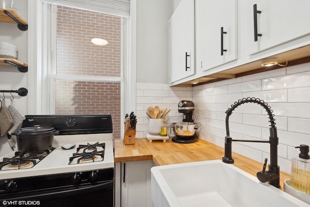 kitchen with a sink, wooden counters, white cabinetry, decorative backsplash, and gas range oven