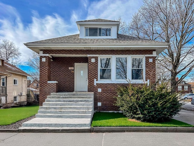bungalow featuring roof with shingles, covered porch, and brick siding