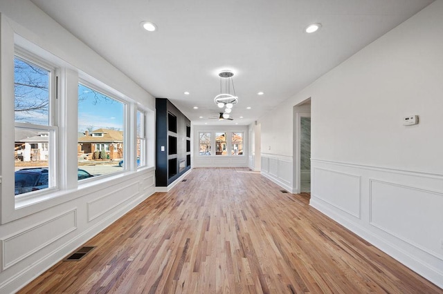 hallway featuring visible vents, light wood-type flooring, a chandelier, and a healthy amount of sunlight