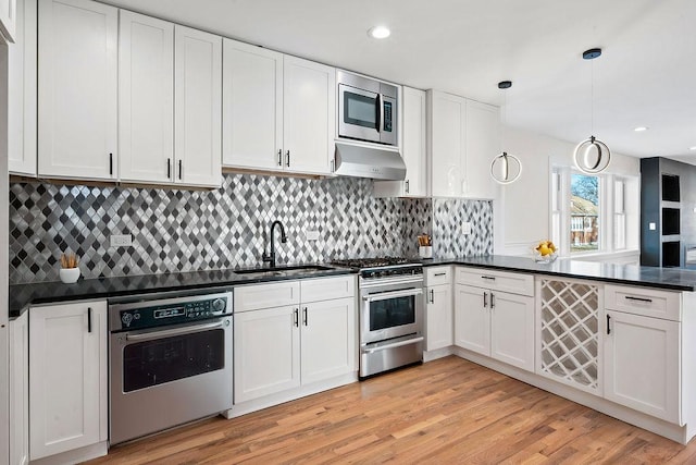 kitchen with dark countertops, under cabinet range hood, appliances with stainless steel finishes, light wood finished floors, and a sink