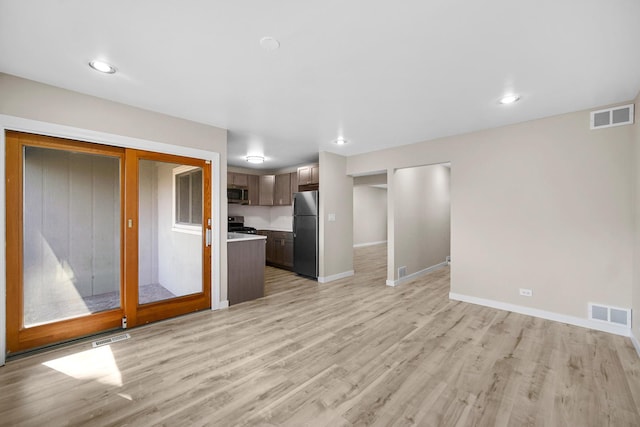 unfurnished living room featuring visible vents, light wood-style flooring, and baseboards