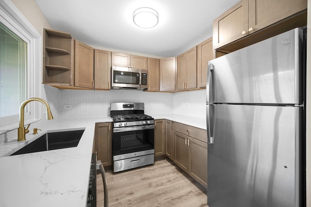 kitchen featuring tasteful backsplash, light stone countertops, light wood-style floors, stainless steel appliances, and a sink
