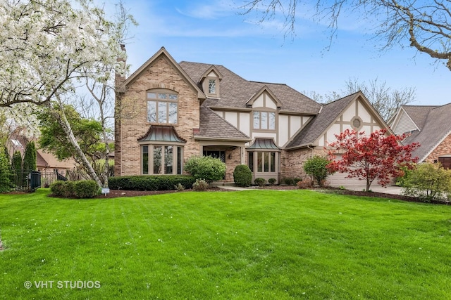 english style home with brick siding, a shingled roof, a front lawn, and stucco siding