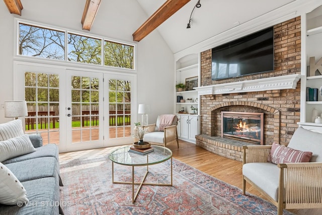 living area featuring french doors, built in features, a brick fireplace, wood finished floors, and beamed ceiling