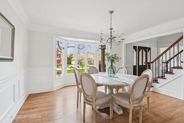 dining room with ornamental molding, light wood finished floors, stairs, and a chandelier