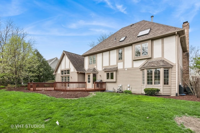 rear view of house featuring roof with shingles, a wooden deck, stucco siding, a chimney, and a yard