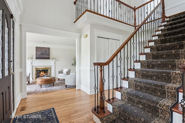 foyer entrance featuring visible vents, wood finished floors, a glass covered fireplace, ornamental molding, and stairs