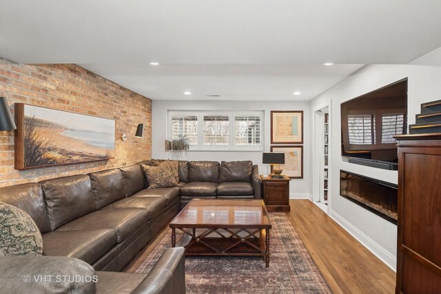 living area featuring wood finished floors, a glass covered fireplace, recessed lighting, built in shelves, and baseboards