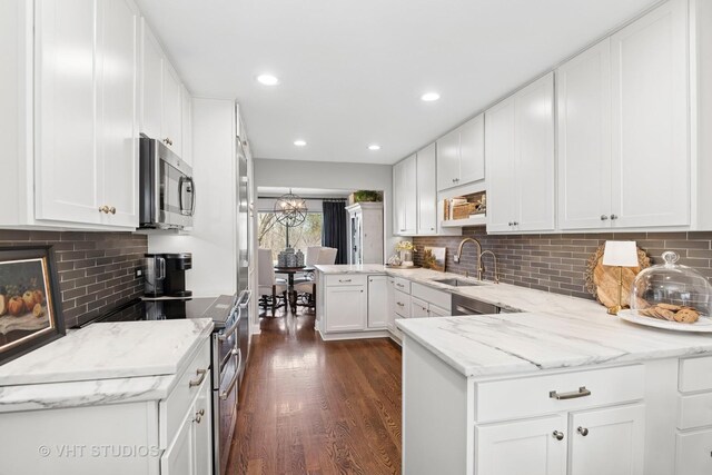 kitchen with appliances with stainless steel finishes, a sink, a peninsula, dark wood-style floors, and white cabinetry