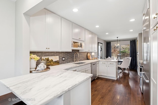 kitchen featuring a peninsula, a sink, dishwasher, white cabinets, and dark wood-style floors