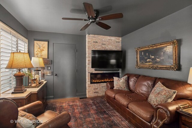 living area featuring a ceiling fan, a large fireplace, wood finished floors, and baseboards