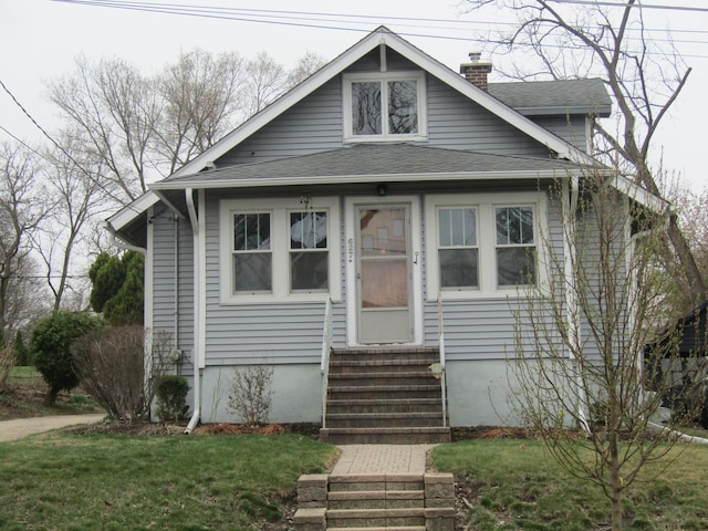 bungalow-style house with entry steps, a chimney, a shingled roof, and a front yard