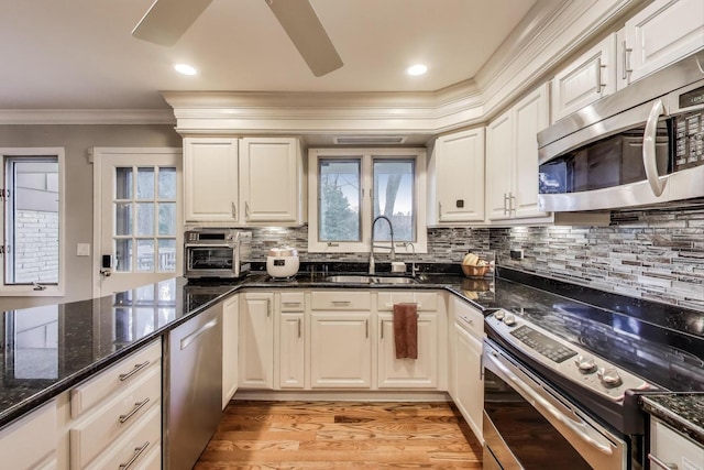 kitchen with tasteful backsplash, a sink, ornamental molding, stainless steel appliances, and light wood-style flooring