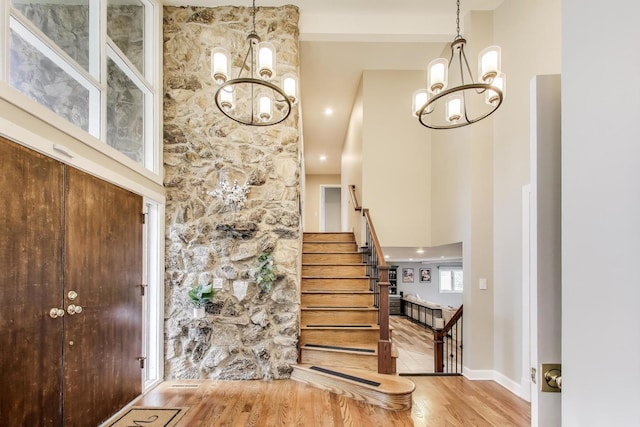 foyer with stairway, a towering ceiling, an inviting chandelier, and wood finished floors
