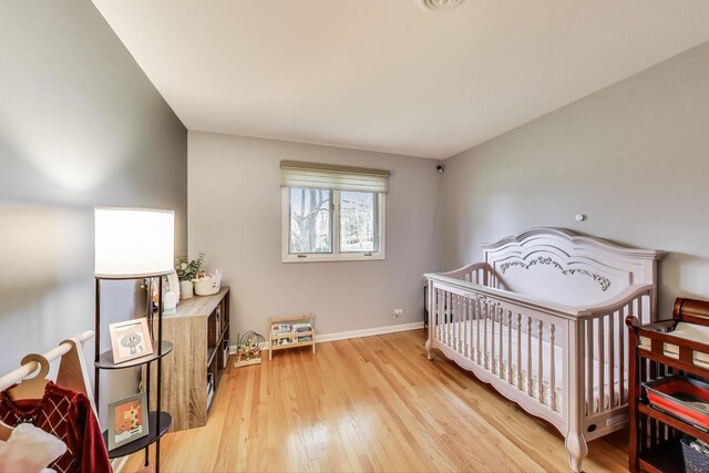 bedroom with a crib, light wood-style flooring, and baseboards
