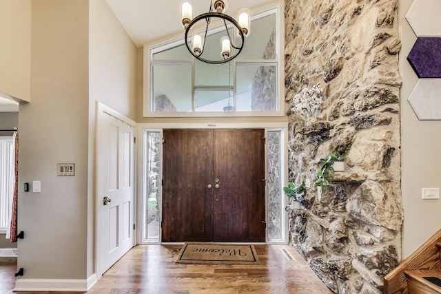 entrance foyer featuring baseboards, high vaulted ceiling, a notable chandelier, and wood finished floors