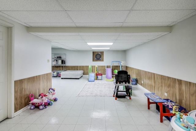 game room with wood walls, a drop ceiling, and wainscoting