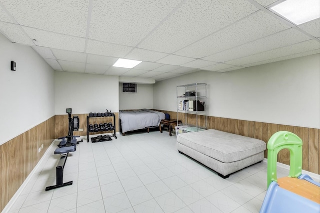 bedroom with wood walls, a drop ceiling, and wainscoting