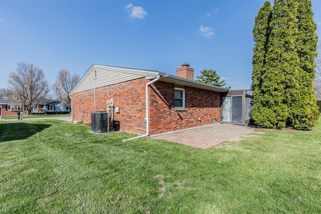 view of side of home with cooling unit, a yard, a patio, brick siding, and a chimney