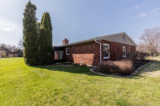 view of home's exterior featuring a chimney, a lawn, and brick siding