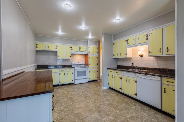 kitchen featuring white appliances, tasteful backsplash, under cabinet range hood, a sink, and dark countertops
