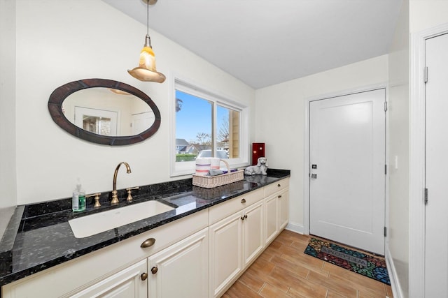 interior space featuring decorative light fixtures, baseboards, a sink, dark stone countertops, and wood finish floors