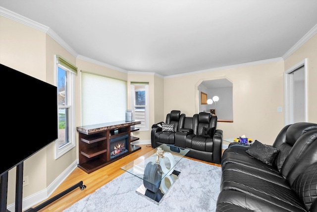 living area with crown molding, light wood-style floors, baseboards, and arched walkways
