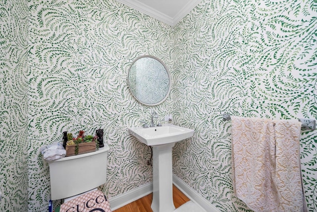 half bathroom featuring toilet, wood finished floors, wallpapered walls, baseboards, and ornamental molding