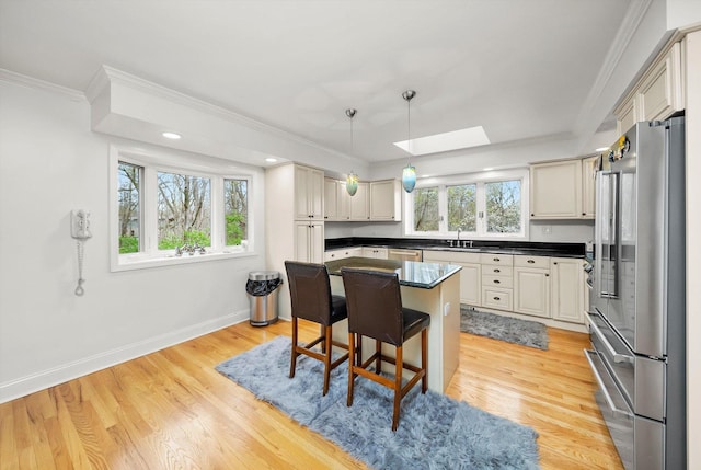 kitchen featuring baseboards, ornamental molding, dark countertops, stainless steel appliances, and a skylight