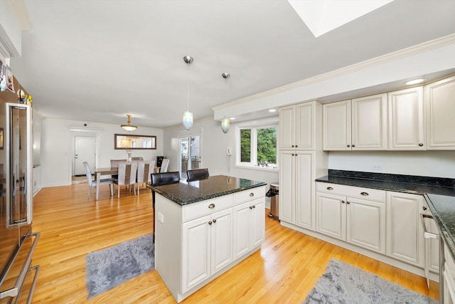 kitchen with a skylight, hanging light fixtures, a kitchen island, and light wood-type flooring