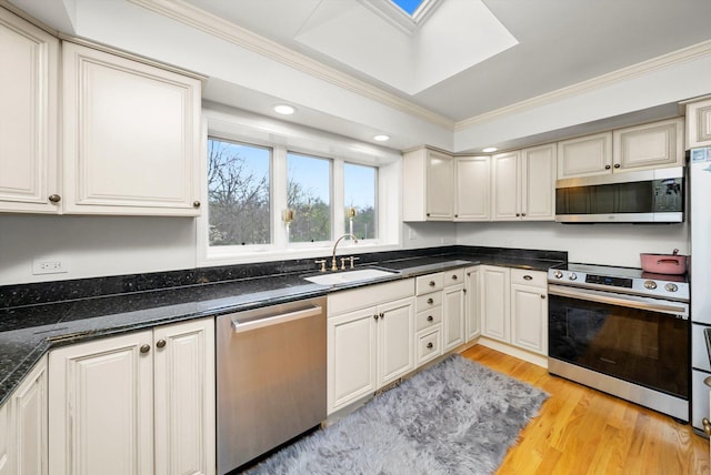 kitchen with light wood-style flooring, ornamental molding, a sink, stainless steel appliances, and a skylight