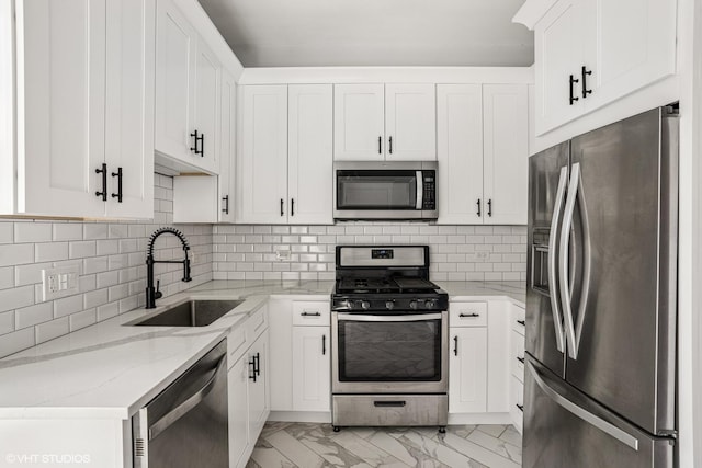 kitchen featuring white cabinetry, light stone countertops, appliances with stainless steel finishes, marble finish floor, and a sink