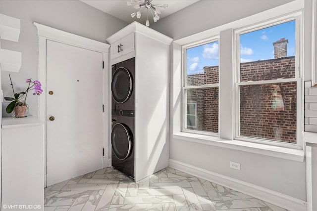 washroom featuring baseboards, marble finish floor, stacked washing maching and dryer, and laundry area