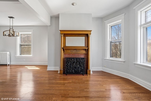unfurnished living room featuring wood finished floors, radiator heating unit, a notable chandelier, and plenty of natural light
