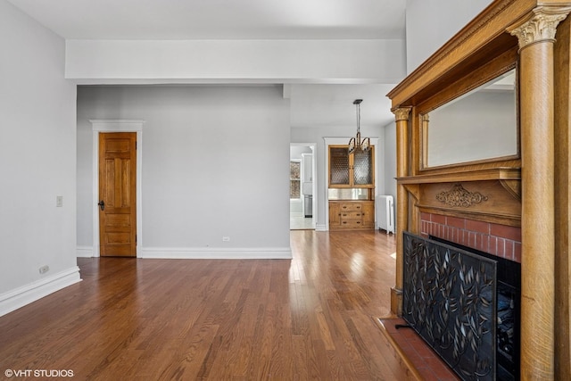unfurnished living room with baseboards, an inviting chandelier, a fireplace, radiator, and dark wood-type flooring