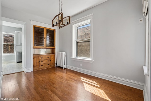 unfurnished dining area with radiator heating unit, baseboards, an inviting chandelier, and dark wood-style flooring