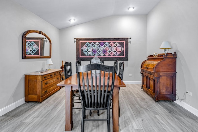 dining space with baseboards, light wood-style floors, and vaulted ceiling
