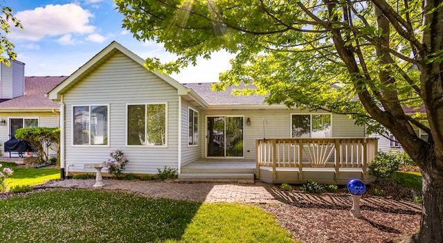 rear view of house with a shingled roof, a deck, and a lawn