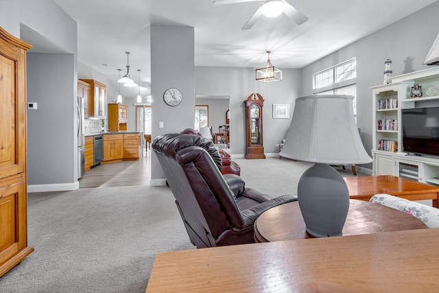 living area featuring light colored carpet, baseboards, and ceiling fan with notable chandelier