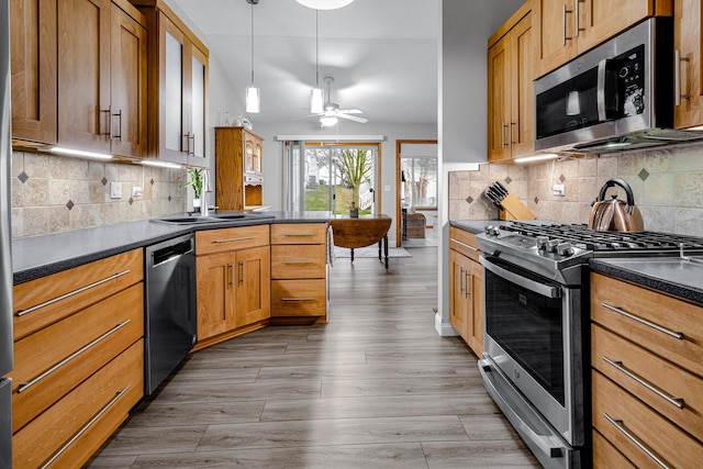kitchen featuring a sink, ceiling fan, dark countertops, stainless steel appliances, and light wood-style flooring