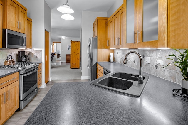 kitchen with appliances with stainless steel finishes, glass insert cabinets, dark countertops, decorative backsplash, and a sink