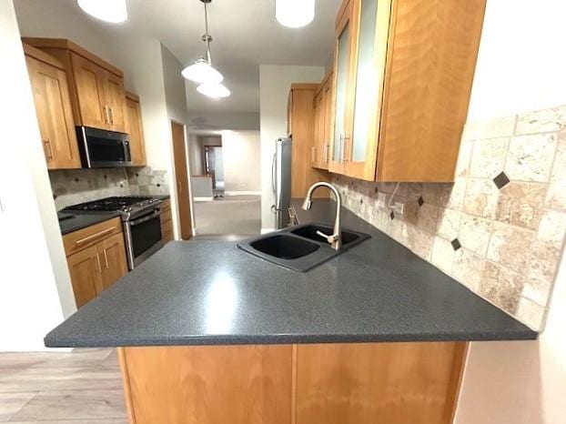 kitchen featuring tasteful backsplash, a peninsula, dark countertops, stainless steel appliances, and a sink
