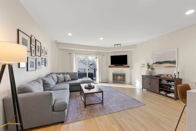 living room with a warm lit fireplace, recessed lighting, and wood finished floors