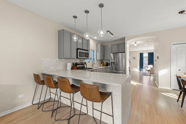 kitchen featuring a kitchen breakfast bar, a peninsula, gray cabinetry, stainless steel appliances, and backsplash