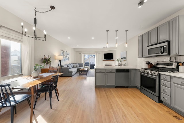 kitchen with stainless steel appliances, gray cabinetry, a peninsula, and an inviting chandelier