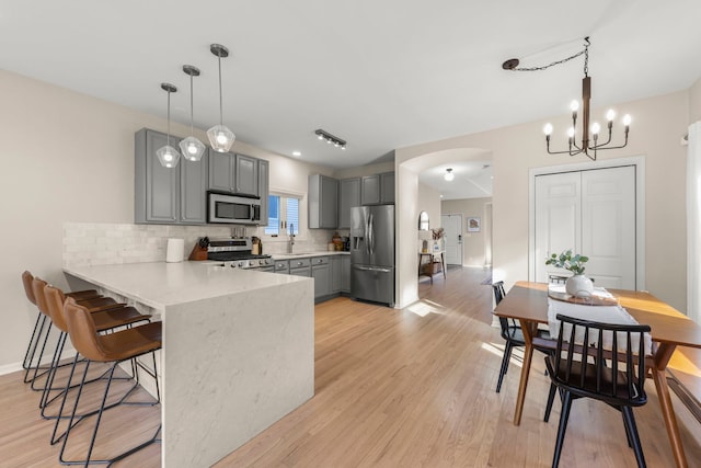 kitchen featuring a kitchen breakfast bar, arched walkways, a peninsula, stainless steel appliances, and gray cabinetry