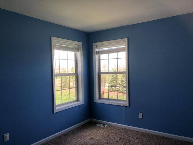 unfurnished room with dark colored carpet, visible vents, plenty of natural light, and baseboards